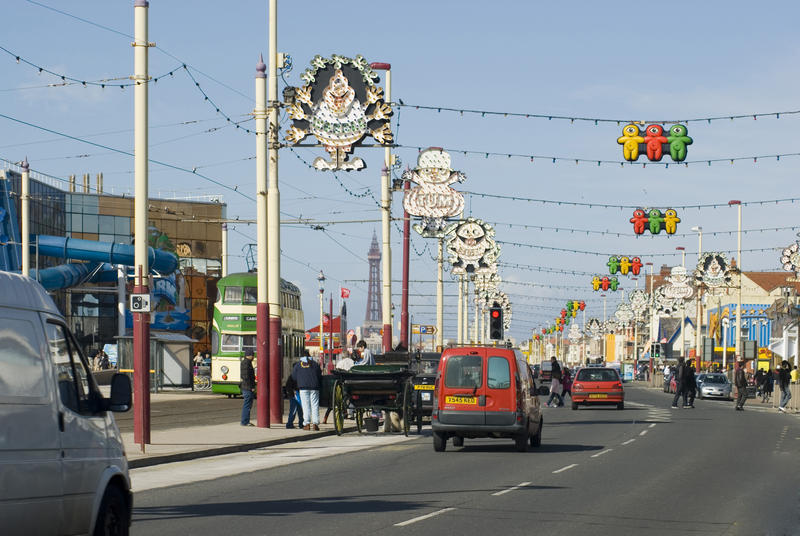 Traffic and people on the Blackpool Promenade with decorative lighting suspended over the road