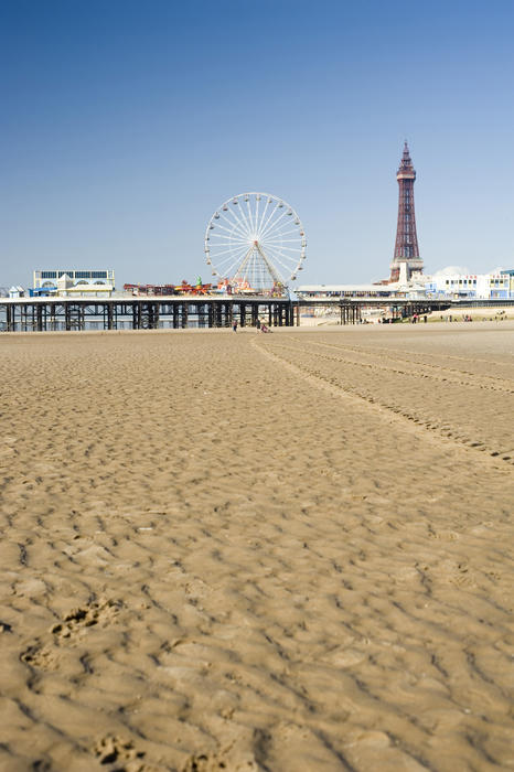 View across wet beach sand at low tide of the Blackpool Tower and Central Pier, Blackpool, England