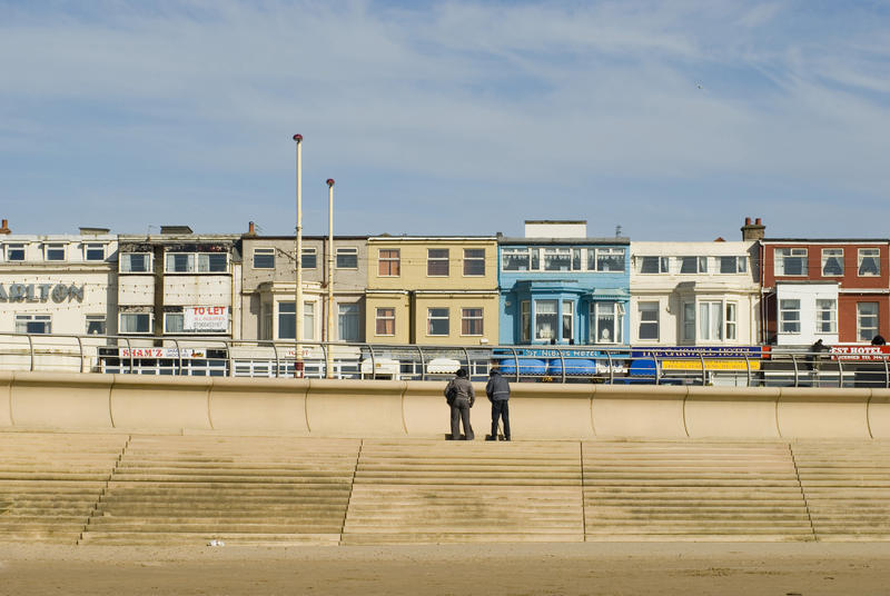 People standing on the steps leading to the beach in front of the Blackpool seafront promenade and buildings
