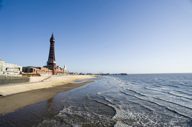 View over a calm ocean and beach to the Blackpool Tower and city waterfront with a pier visible in the distance