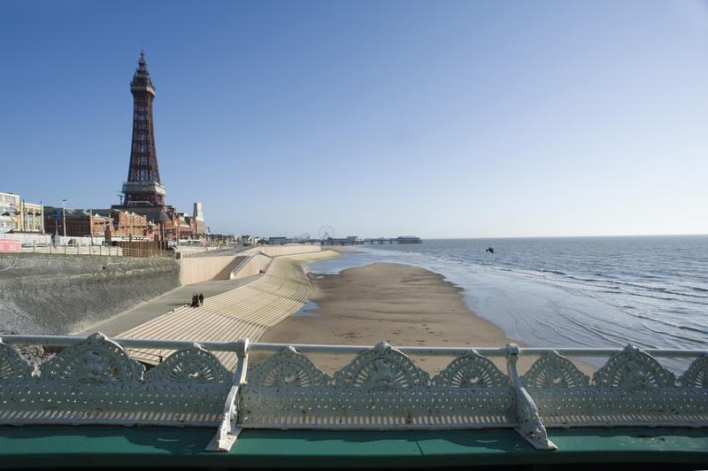 View looking over the balustrade of the North Pier of the historical Blackpool Tower and beach with a section of the city waterfront visible behind