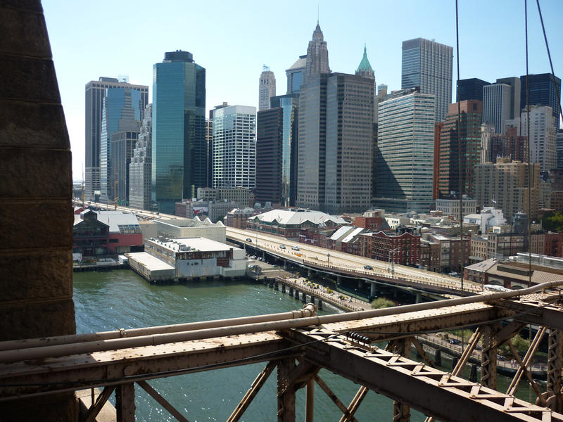 View of the Manhattan waterfront skyscrapers against a blue sunny sky from Brooklyn Bridge with a section of the framework in the foreground