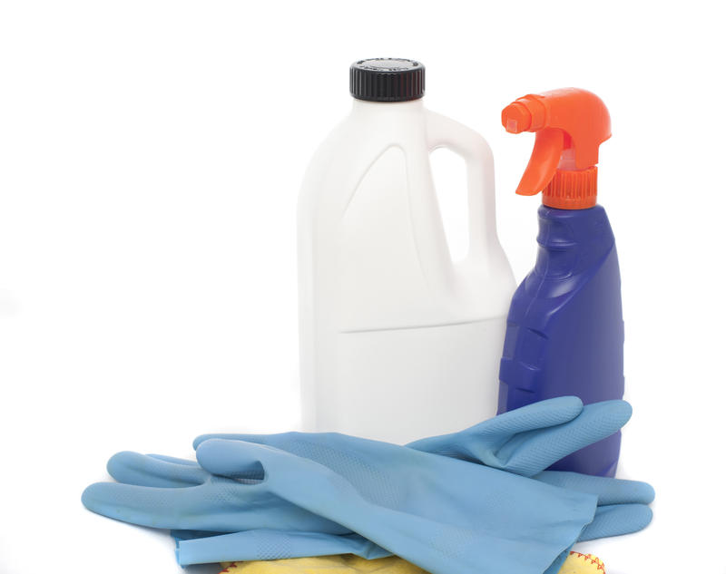 Various household cleaning products ready for use including a cloth, gloves, a spray bottle and disinfectant over white