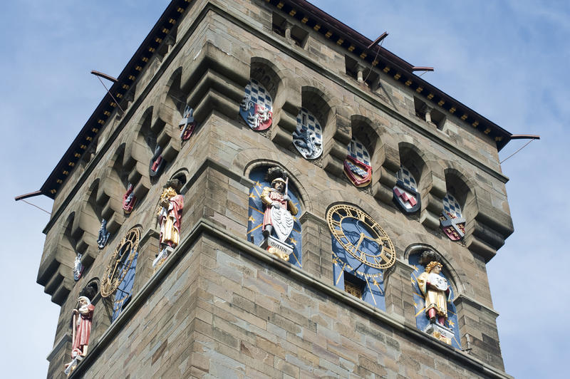 Clock tower at Cardiff Castle designed by William Burges with a gilded clock on each face and sculptures representing the planets below armorial shields