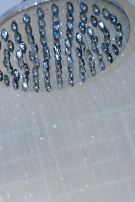 Close-up of shower head with water drops and white tiles