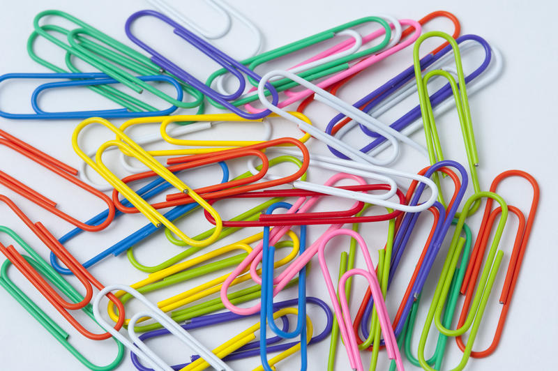 Abstract background of scattered colourful paperclips on white
