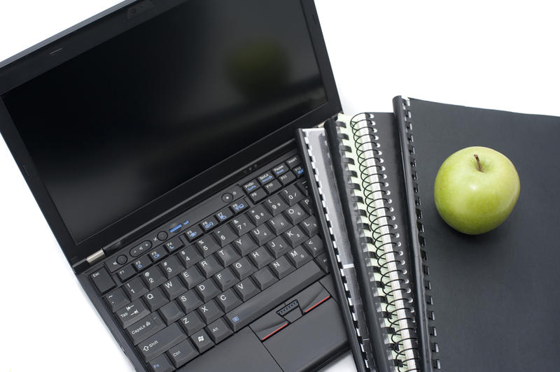 Computer education and learning concept with an open laptop lying beside a set of sprial bound notebooks topped with a healthy green apple