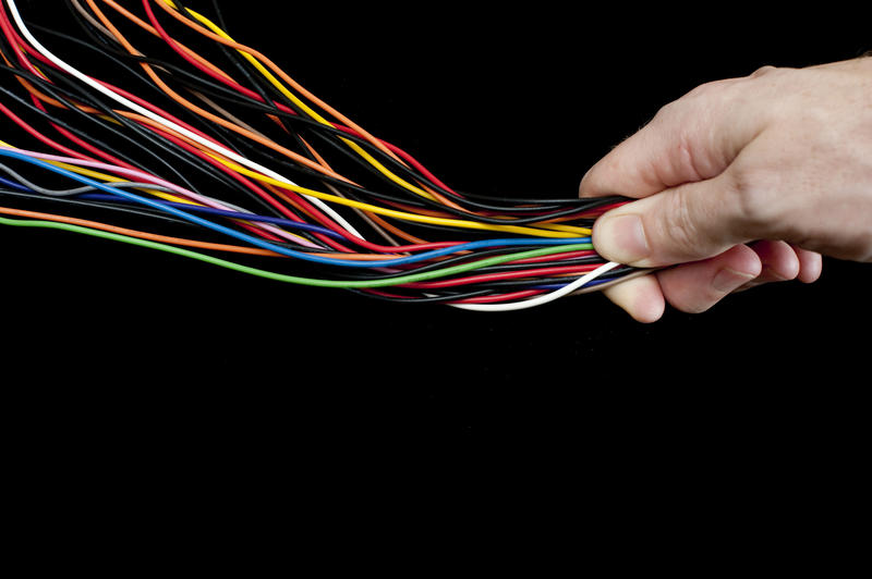 Multiple multicoloured electric wires in a diverging tangle are constrained and controlled under the thumb of a man