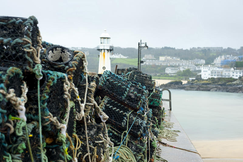 Lobster pots in the fishing town and holiday resort of St Ives harbour, Cornwall, stacked high on the quayside with the top of the lighthouse visible behind