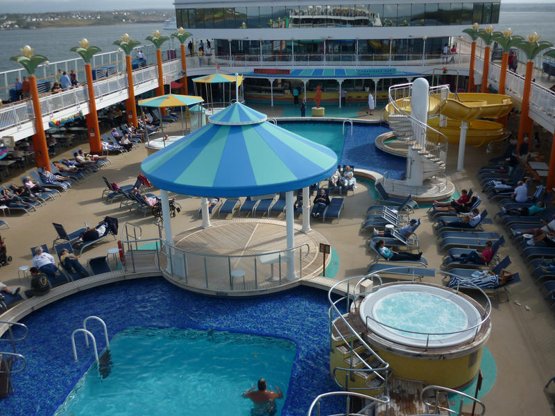 Swimming pool and sundeck on a cruise liner with tourists relaxing in the sun while on a holiday voyage