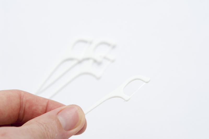 Man holding a disposable plastic flossing pick loaded with a length of dental floss for cleaning between his teeth