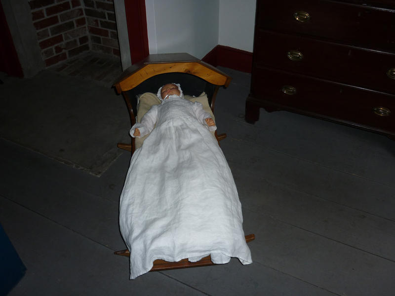 Antique doll lying in a wooden crib on an exhibit, view down the length of the crib