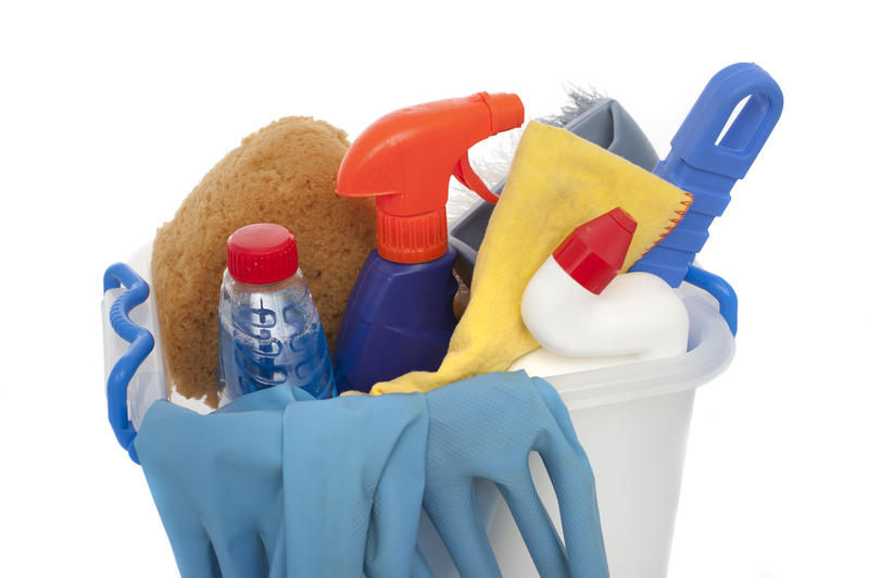A studio shot over white of a bucket of domestic cleaning products with rubber gloves and sponges