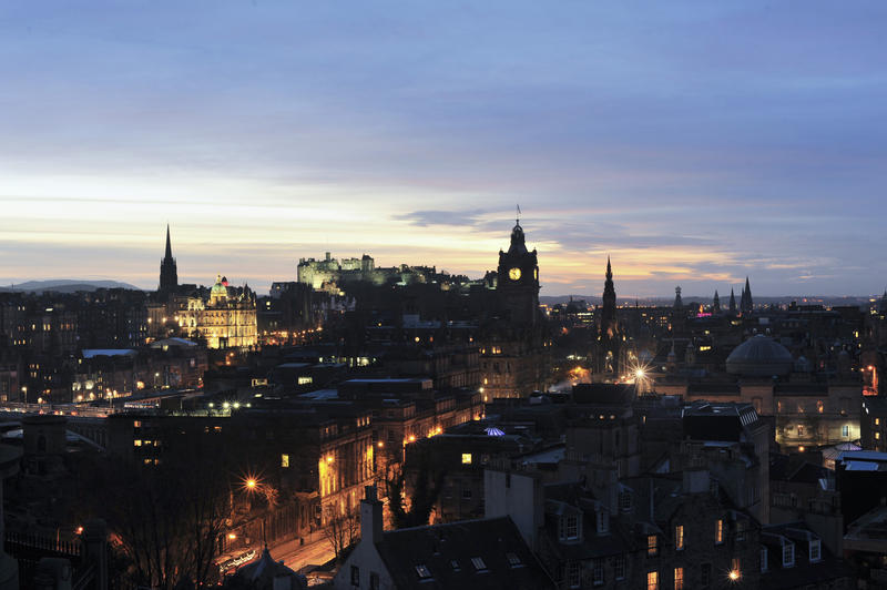 Edinburgh at night with a view across a brightly lit Princes Street to the Edinburgh Castle and Rock floodlit on the skyline