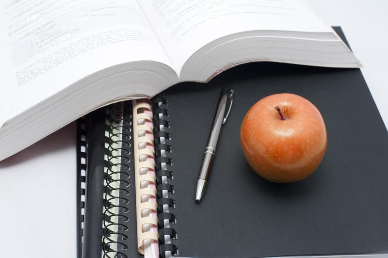 Educational and diet concept with a fresh red apple for a healthy snack standing on top of spiral bound notebooks alongside an open textbook