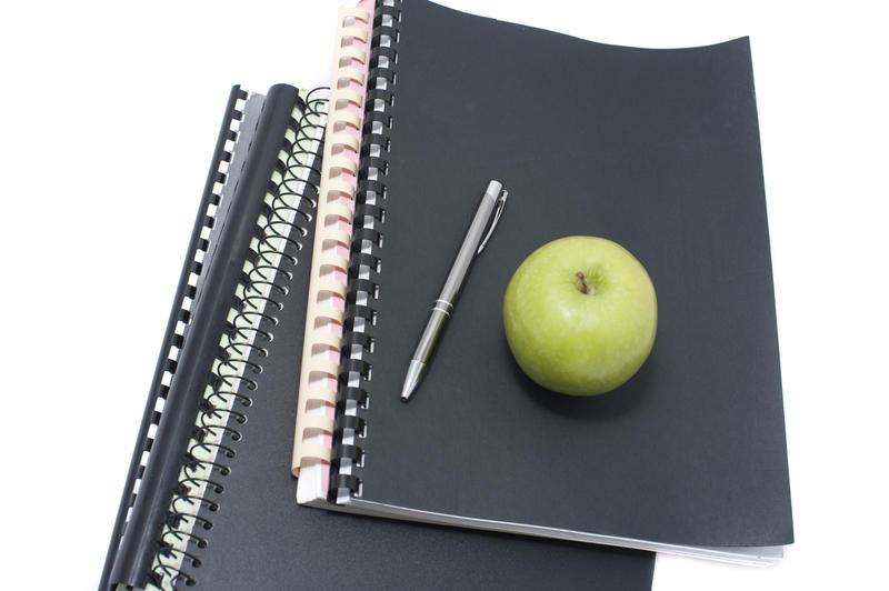 Fresh green apple and pen on lying on a stack of spiral bound notebooks in an education concept