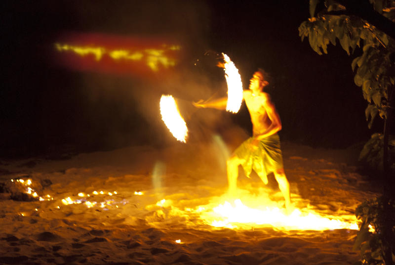 Fijian fire dancer performing on the beach twirling flaming torches in traditional moves lit by flames on the ground