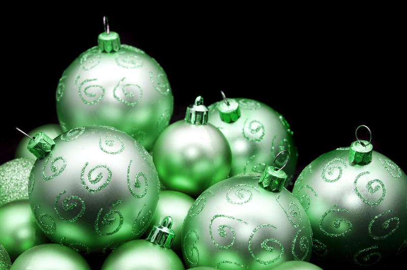 Pretty shiny green Christmas baubles with glitter decoration against a dark background with copyspace for your festive wishes