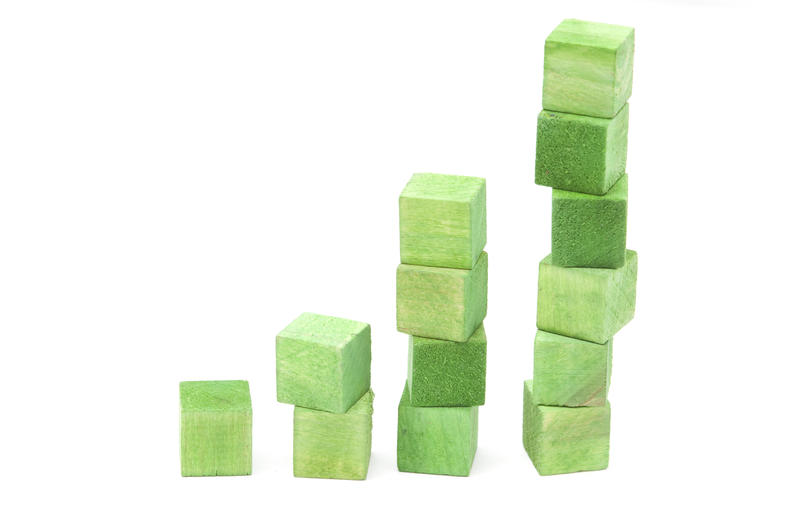 Growth concept using green wooden toy building blocks stacked in increasing numbers on a white background