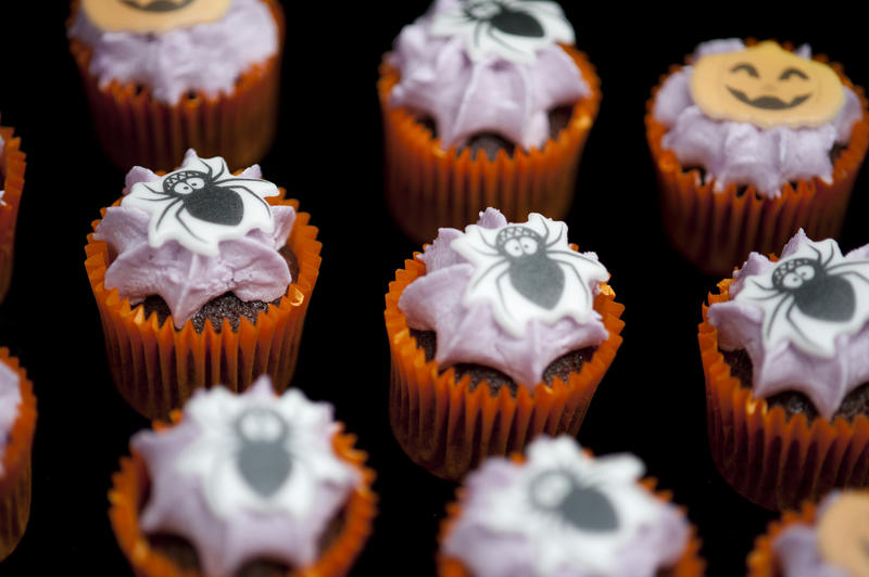 an array of miniature party cakes with icing and spider decorations on top