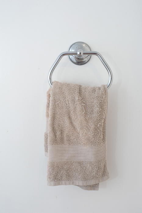 Beige hand towel hanging in a bathroom from a stainless steel wall mounted fixture in a health and personal hygiene concept