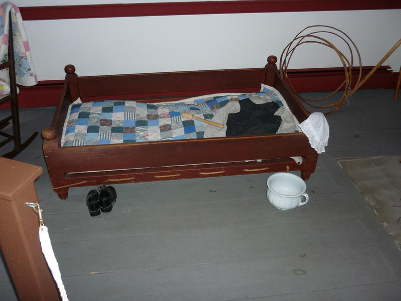 Historic childs cot with a wooden frame and duvet with tiny boots, a night cap and potty in a museum exhibit