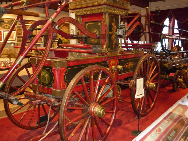 Antique red fire pump engine with large spoked wheels restored and exhibited in a museum showing fire engines through the ages