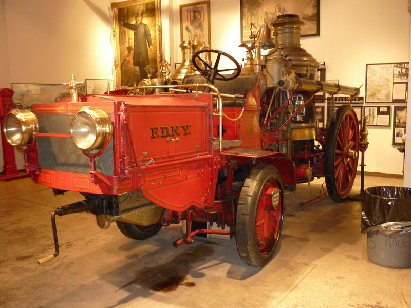 Historic red firetruck on display with a crank handle, steam engine and old spoked metal wheels