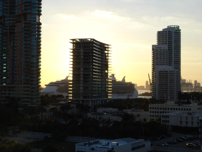 Huge luxury passenger liner cruise ship in Miami at sunset seen between skyscraper buildings as it prepares to set off on an ocean voyage