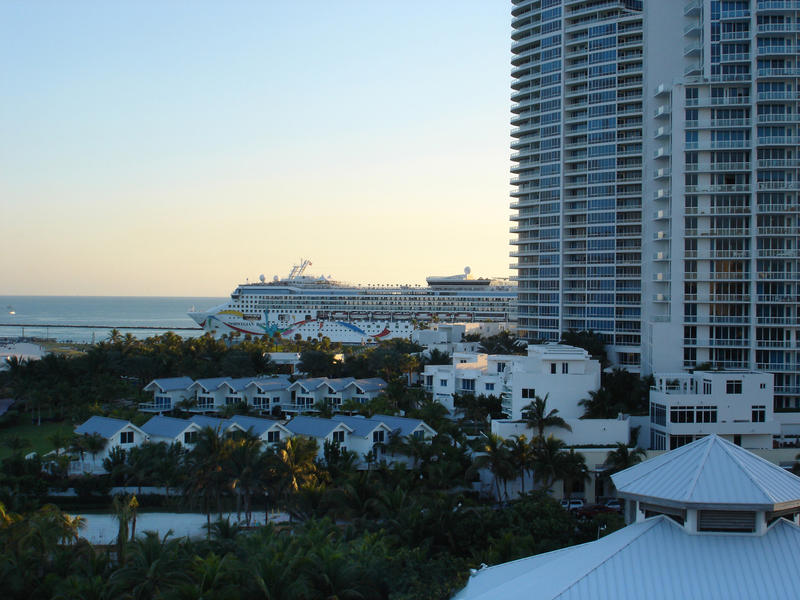 Large luxury cruise liner in Miami visible over the rooftops against a glowing sunset sky