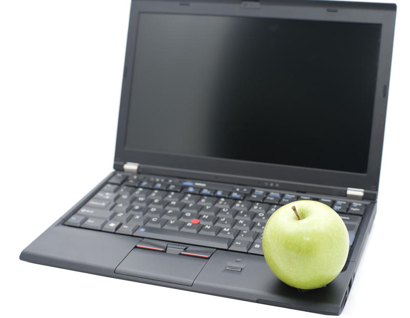Modern education concept with a healthy green apple balanced on the open keyboard of a laptop computer