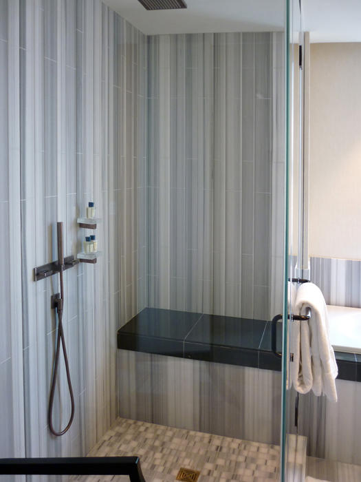 Modern glass shower cubicle with a tiled floor, interior seat and a towel hanging on the door in an interior decor and personal hygiene concept