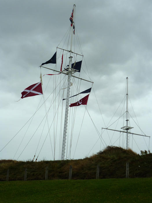 Nautical flags hoist on a tall flagpole flying in the breeze under a grey cloudy sky