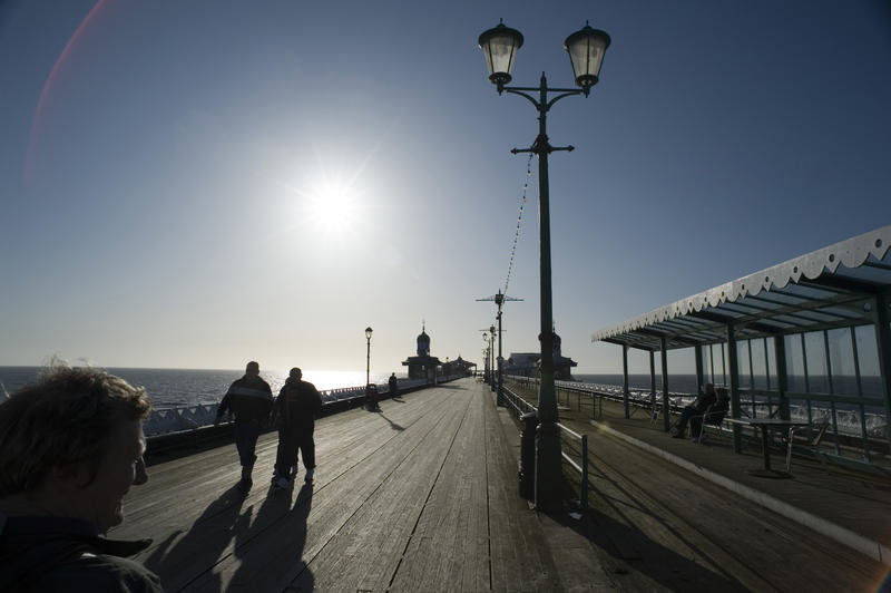 People walking along the wooden broadwalk on Blackpool North Pier silhouetted against the sun
