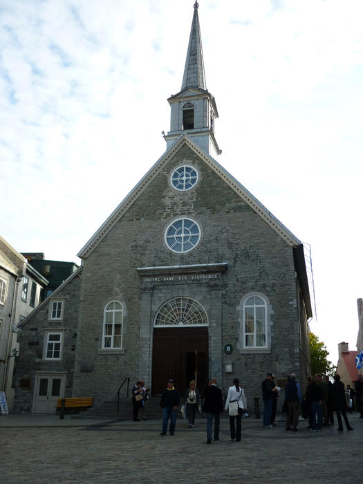 The quaint stone building of Notre Dame church, Quebec city with members of the congregation standing outside in the street