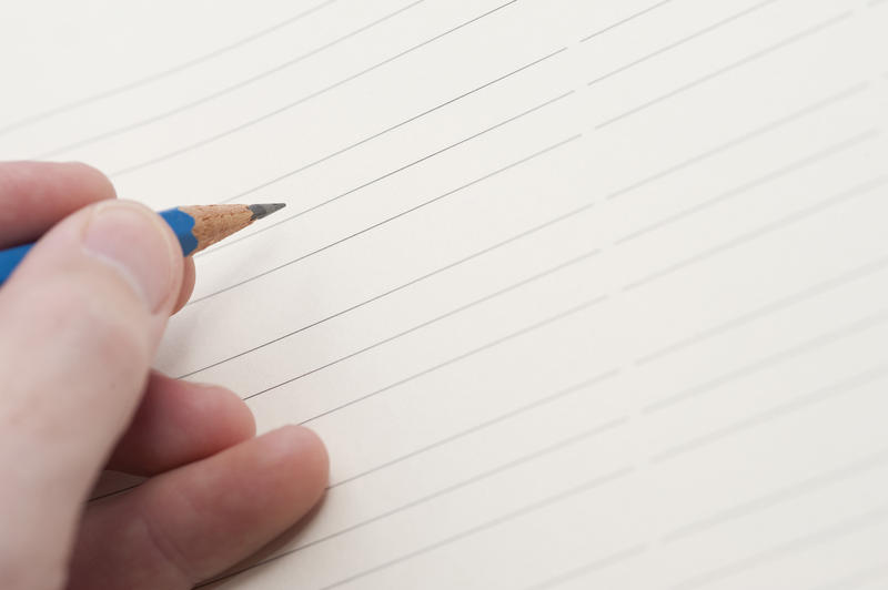 Male hand holding a pencil ready to commence writing on a blank lined sheet of paper