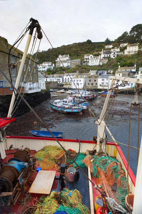View of the harbour and traditional white-washed cottages in Polperro fishing village, Cornwall with a colourful collection of nets and equipment on the deck of a fishing boat in the foreground