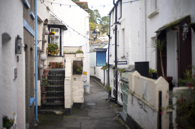 View up a narrow pedestrian lane between traditional white-washed cottages in Polperro fishing village, Cornwall, a popular tourist attraction