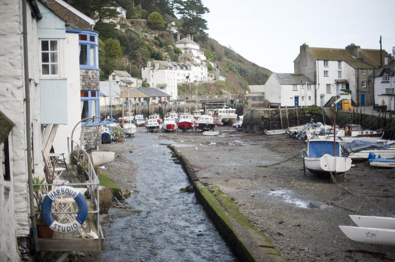The quayside at Polperro fishing village, Cornwall with a fleet of small fishing boats beached on the sand and quaint unspoilt white-washed cottages