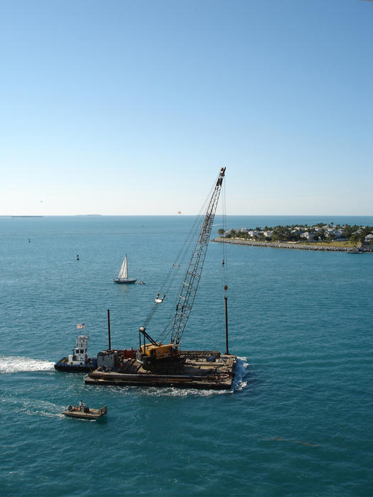 Large industrial floating crane being transported by sea on a large pontoon being guided by tugs