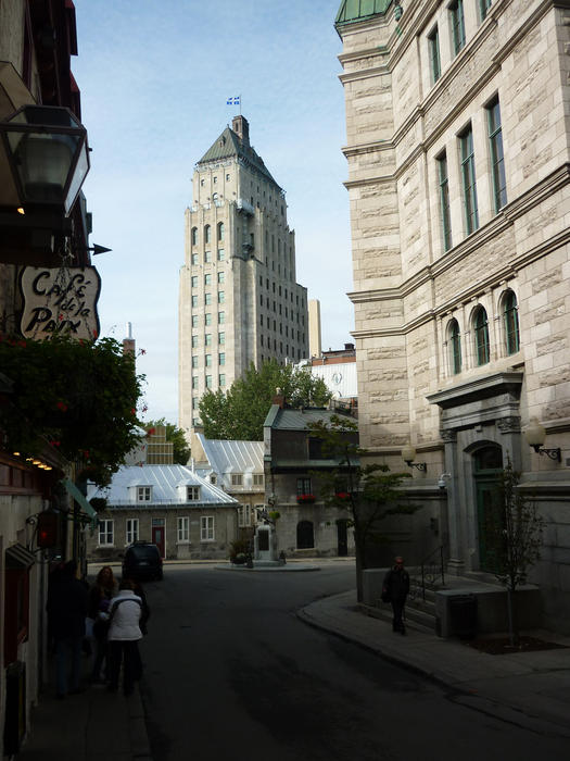 View down a narrow street past a historical stone building facade to an unusal highrise building typical of Quebec City architecture