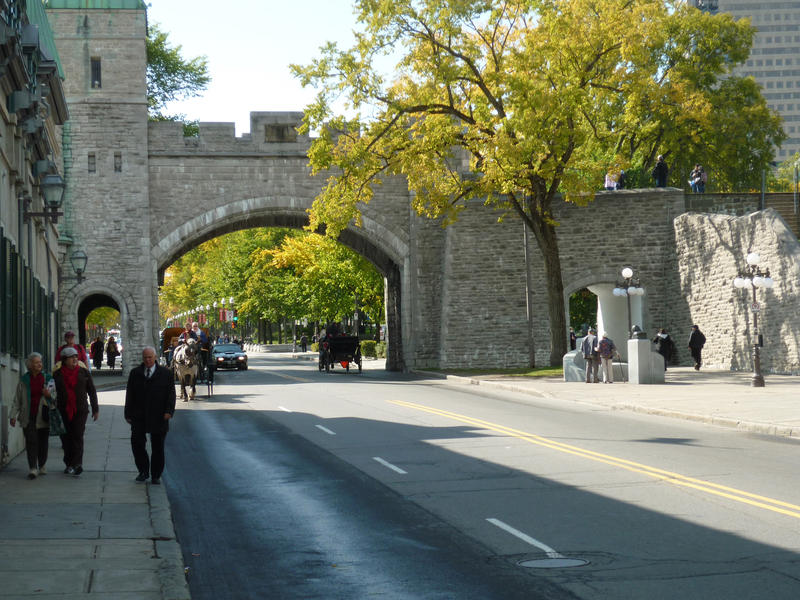 Old historical stone ramparts of Quebec City with a dual lane road running through the archway and pedestrians strolling on the sidewalks