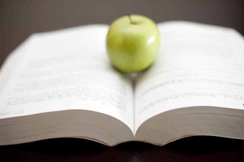 Green apple positioned on the pages of an open book. Selective focus