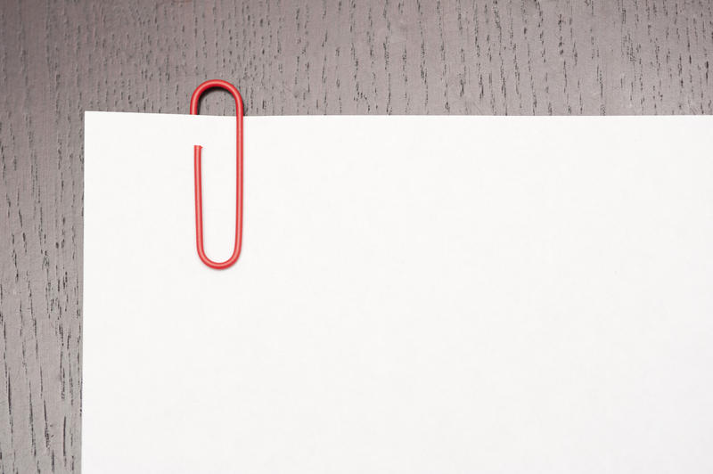 sheet of white paper on brown desk with red paper clip