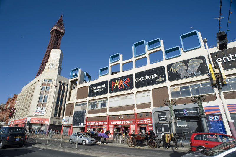 Busy street scene in Blackpool on the waterfront with traffic and people in front of commercial buildings with the Blackpool Tower just visible behind