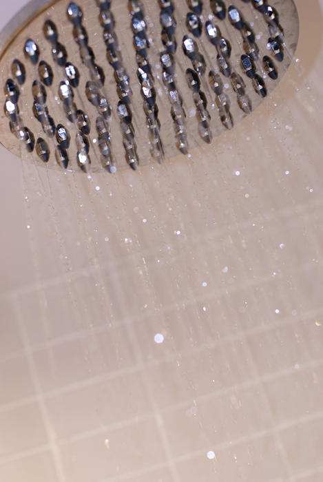 Partial view of a shower head and water drops in a shower with white square tiles