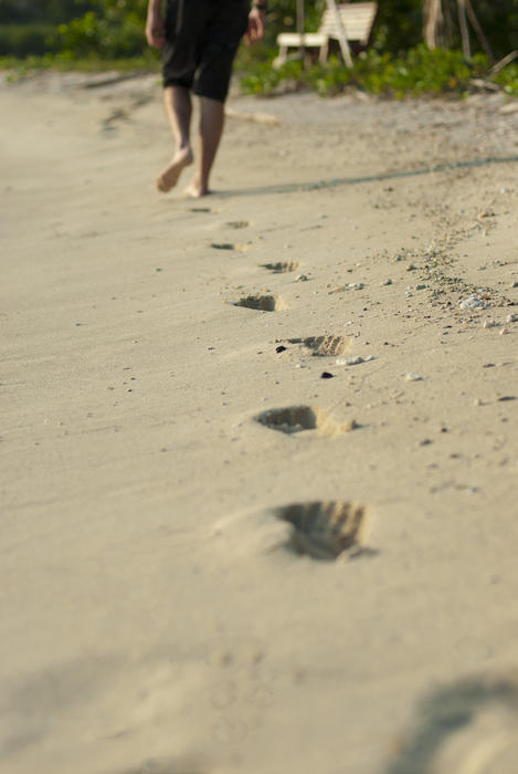 Person walking away across a beach leavng barefoot footprints in the sand during a walk on a sunny summer day on vacation