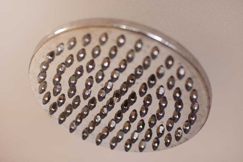 Closeup of a large round stainless steel shower head bathroom fixture with multiple small nozzles