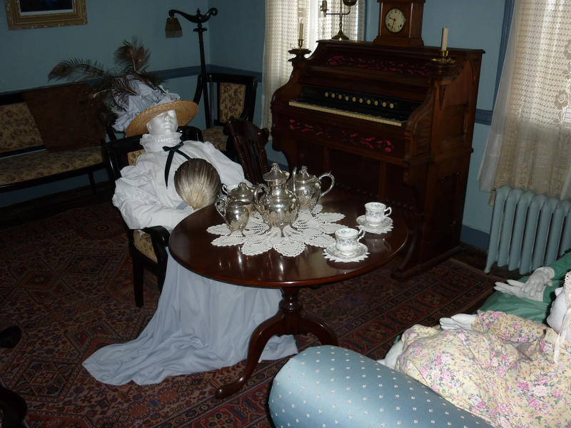 Museum exhibit of the interior of a Victorian or Edwardian parlour with a lady entertaing her friend with a silver tea service