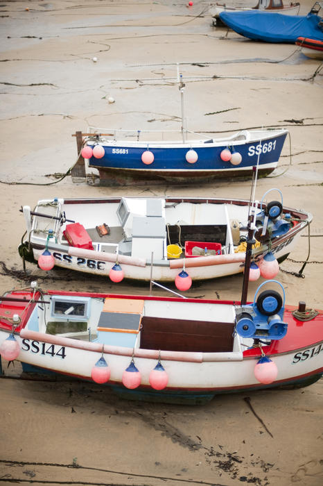 Small fishing boats hung with fenders stranded on the sand at low tide in St Ives harbour, Cornwall